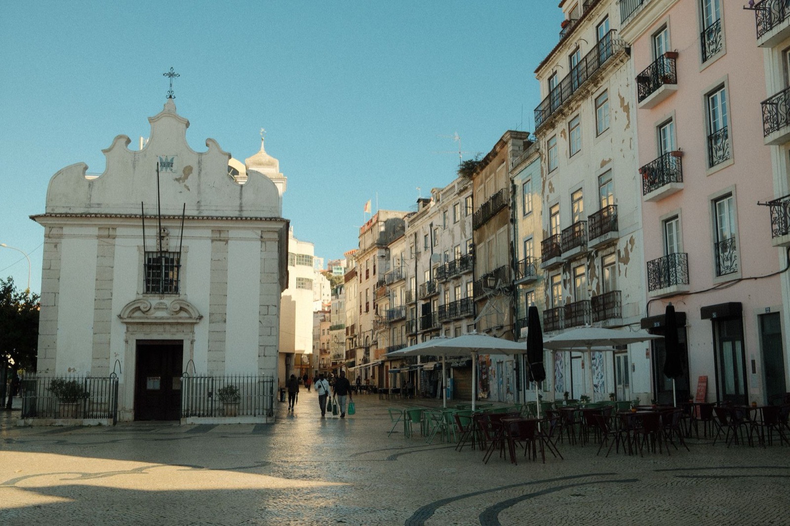 A quiet Lisbon square with traditional residential buildings, Portuguese pavement and a neighbourhood café.