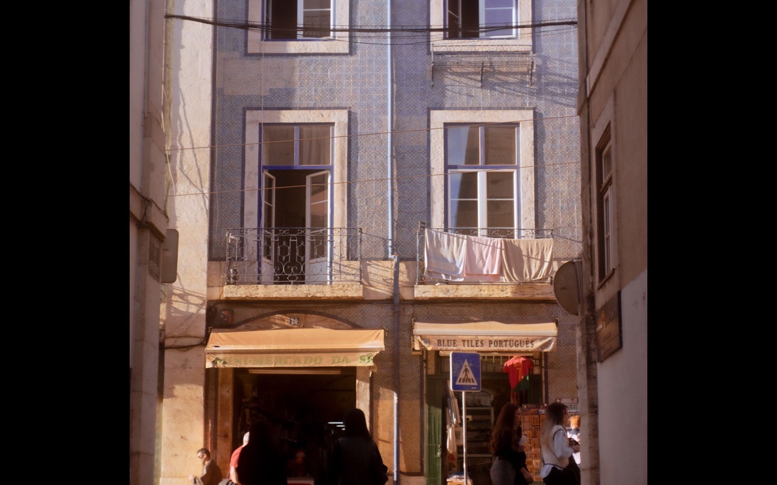 A Lisbon neighbourhood street with tiled building facades and everyday local shops.